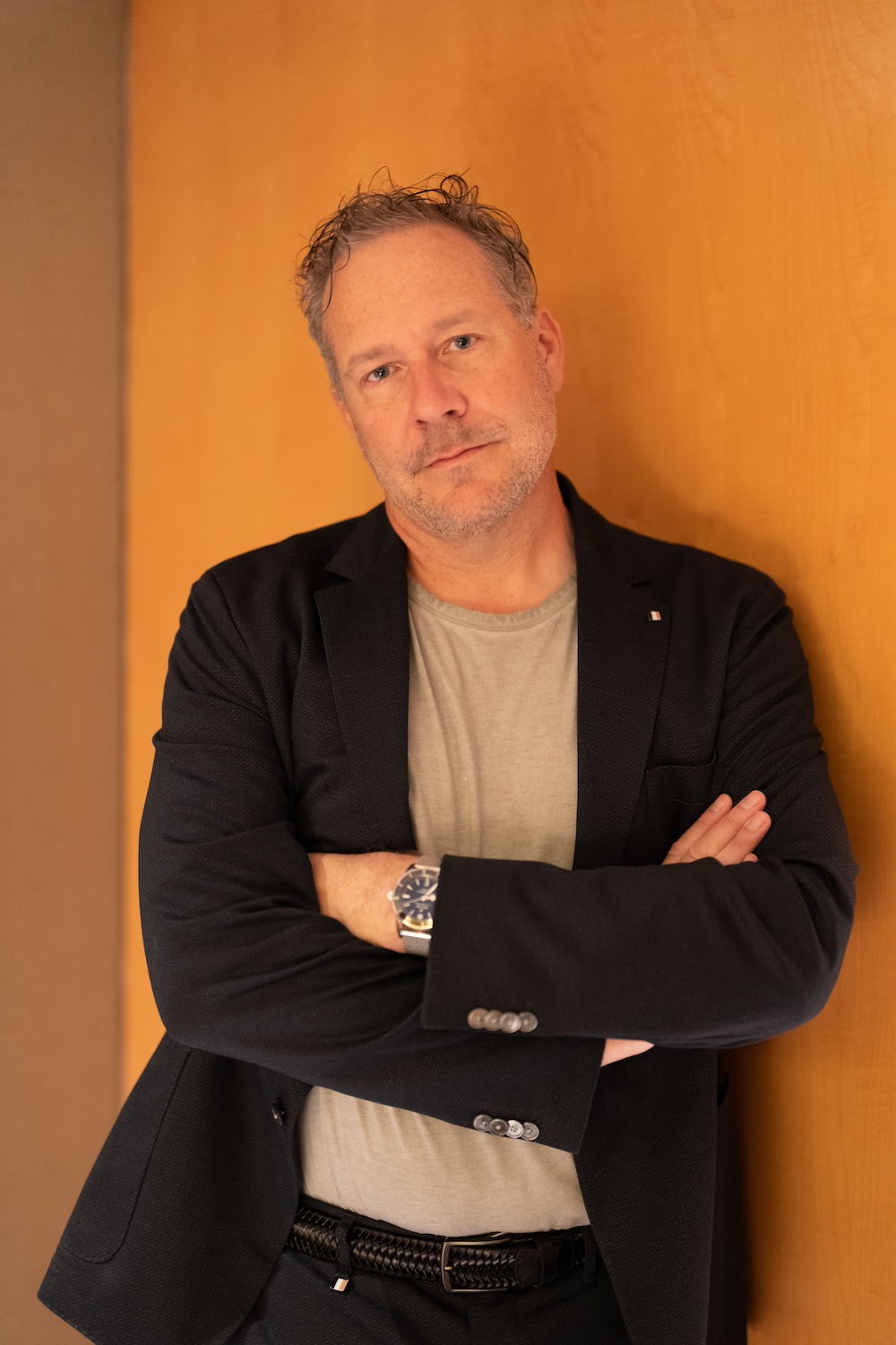 Douglas Gourlay standing against a warm wood wall, wearing a dark jacket with his arms crossed