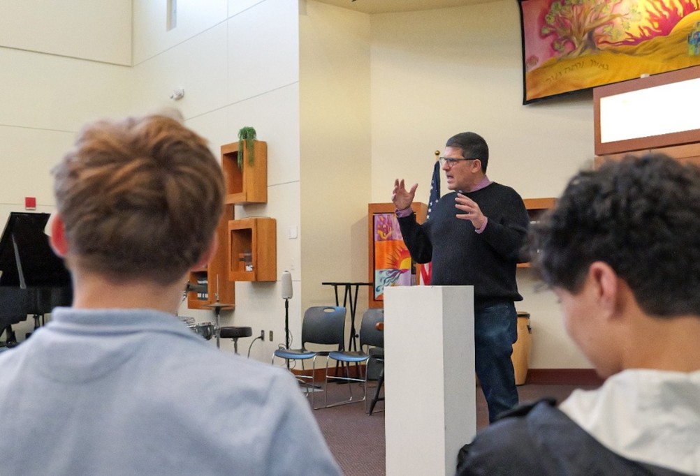 Douglas Levin speaking to students at Gann Academy, gesturing beside a lectern