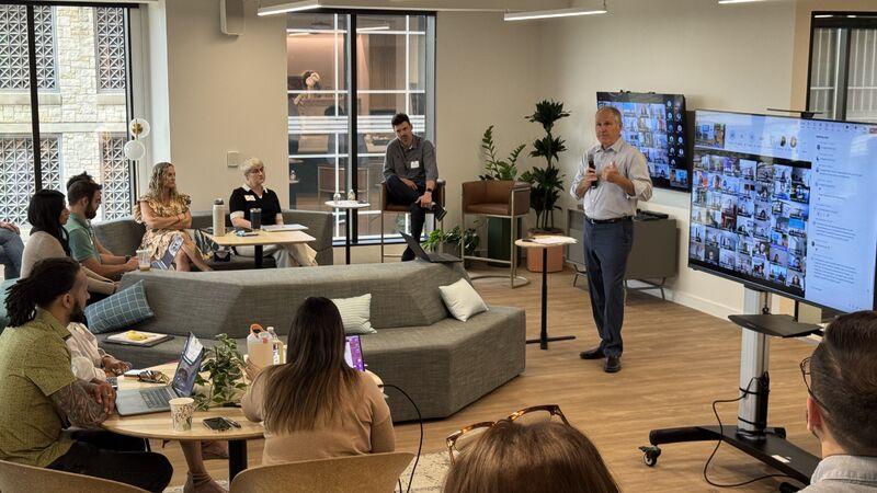 Douglas Valenti speaking to colleagues in a Modernize office lounge, with remote participants on a screen