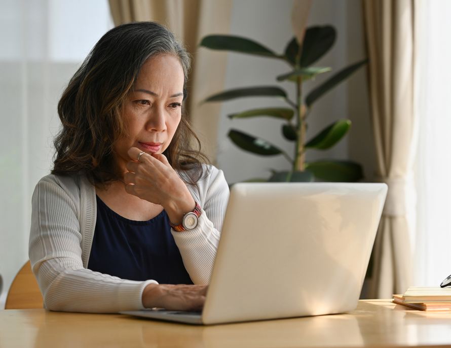 A woman concentrating on a laptop at a sunlit table