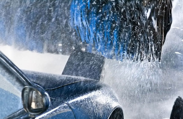 A blue car passes beneath wet brushes in a car wash