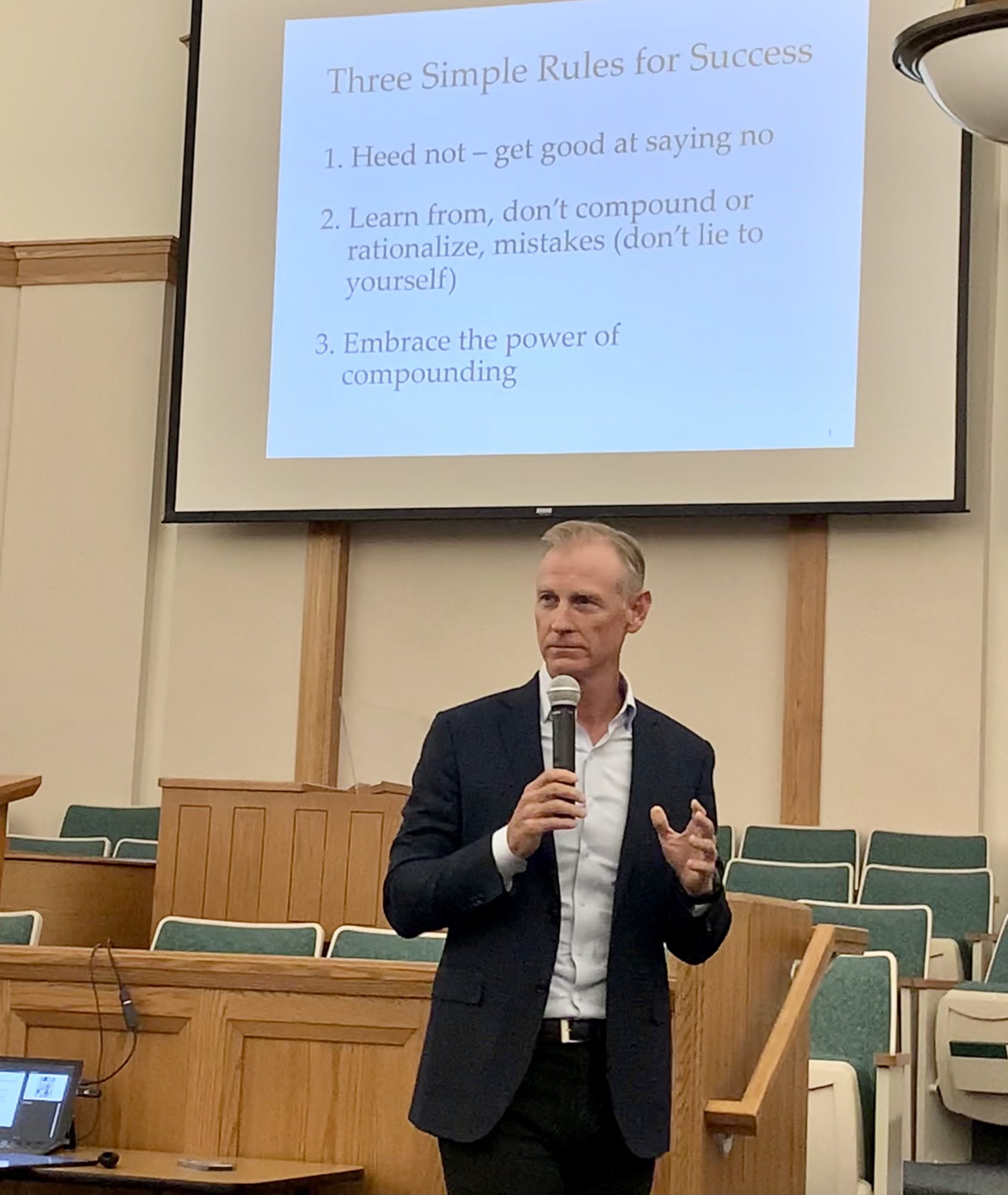 Drew Johnson speaking into a microphone at the 2022 DFW Leadership Series, beneath a slide outlining three rules for success