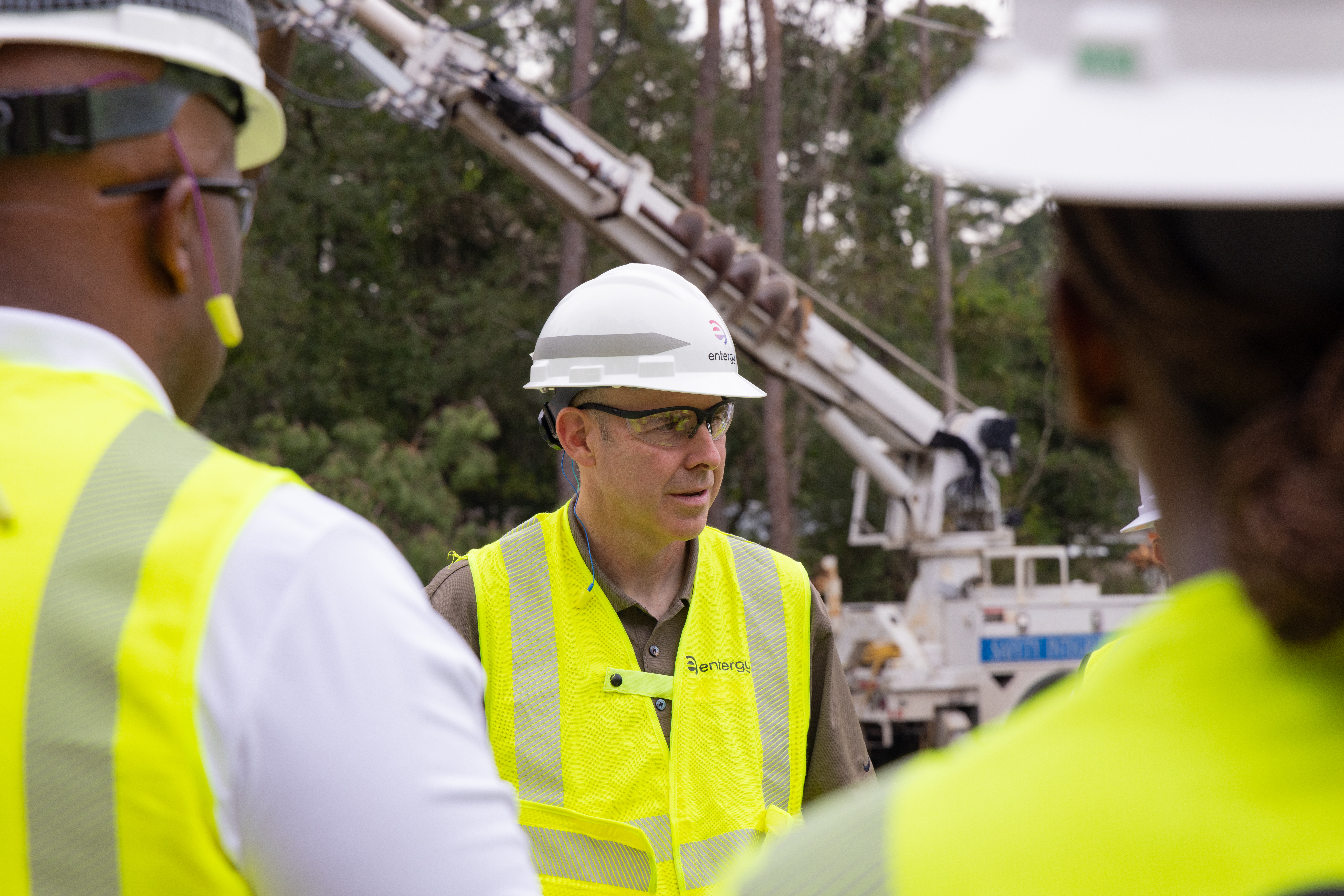Drew Marsh, in a hard hat and reflective vest, speaks with colleagues beside utility equipment.