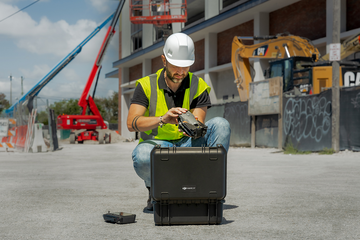 A construction worker surveys a site while a professional drone flies overhead