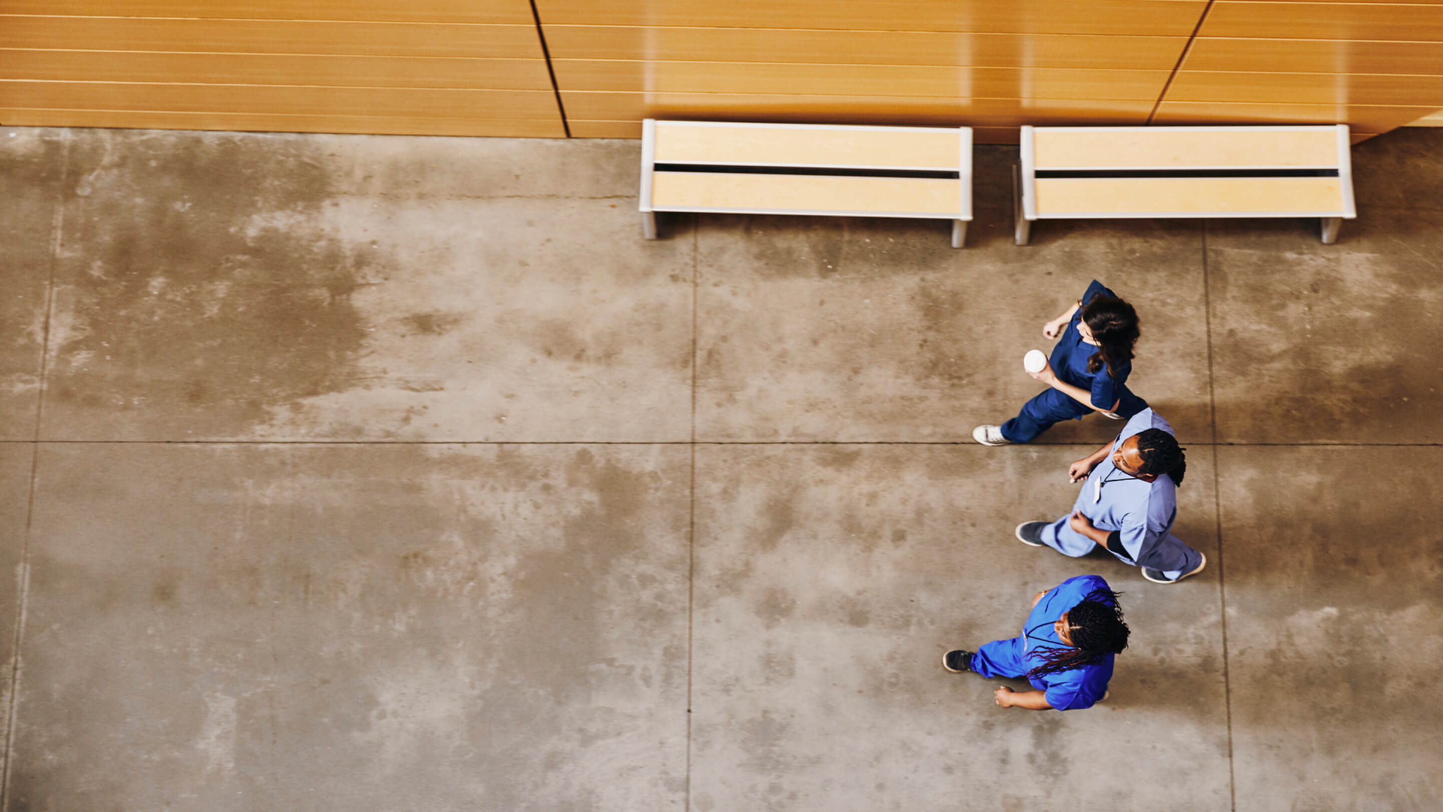 Three clinicians in scrubs walking through a hospital corridor, seen from above