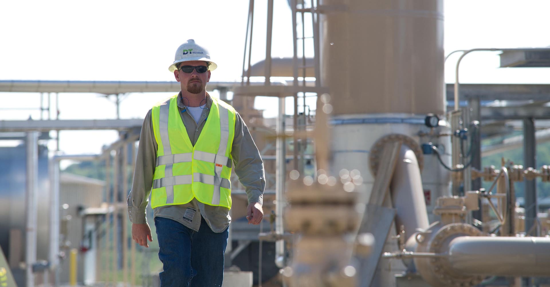 A DT Midstream employee in a hard hat and high-visibility vest among operating equipment