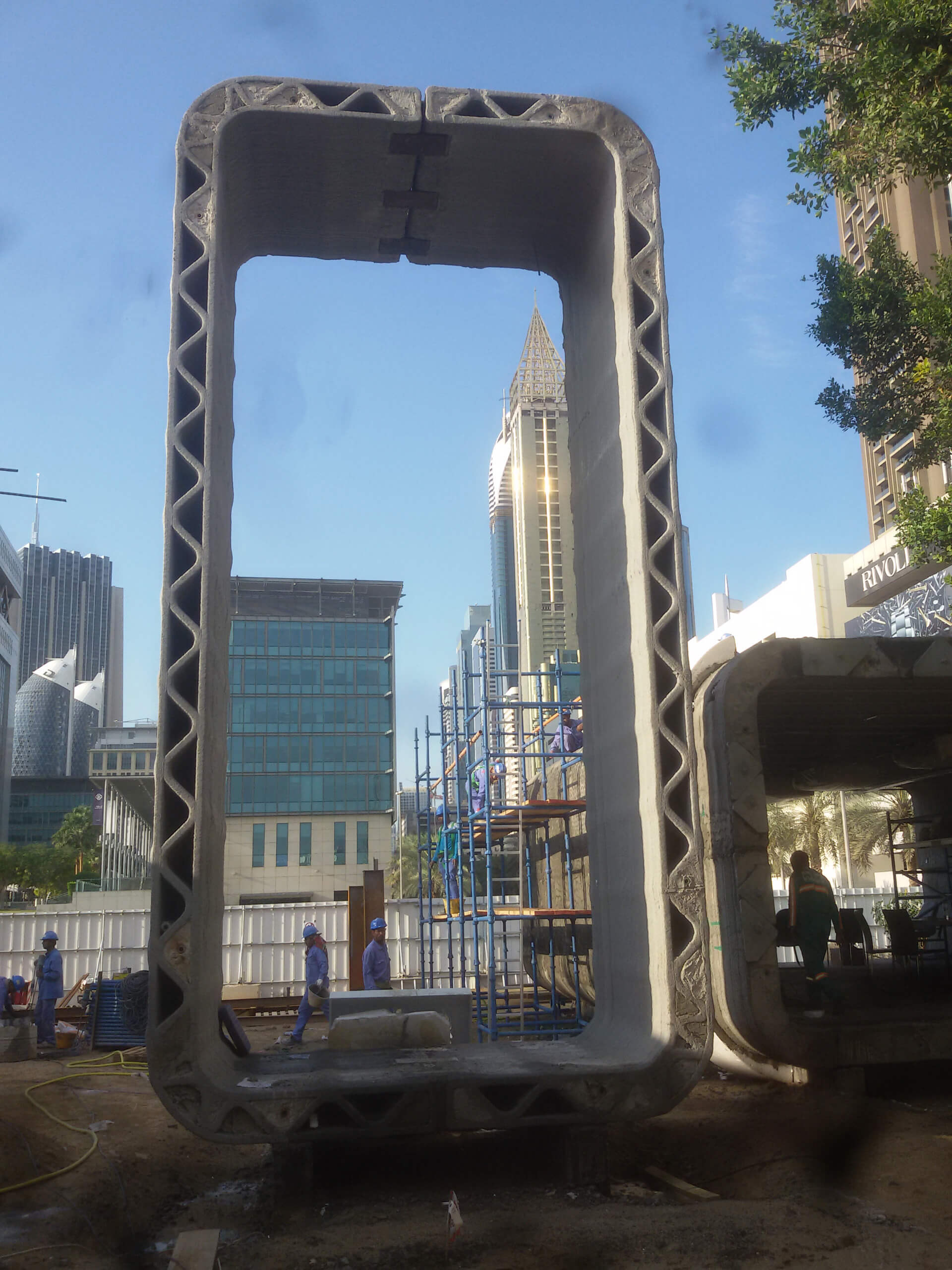 A tall printed concrete element being assembled, with workers and scaffolding below