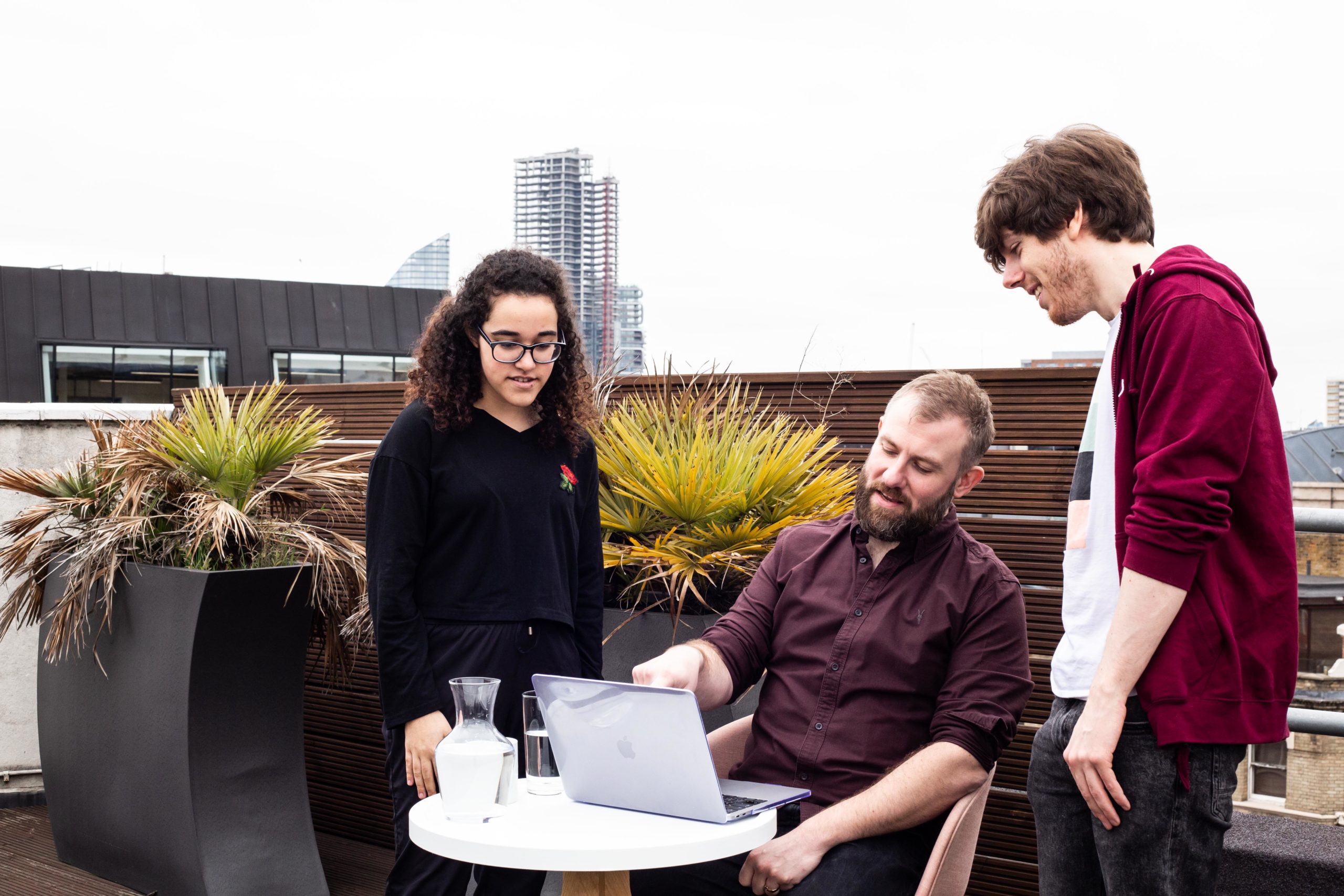 Three people gathered around a laptop on an outdoor terrace in Duco’s careers photograph