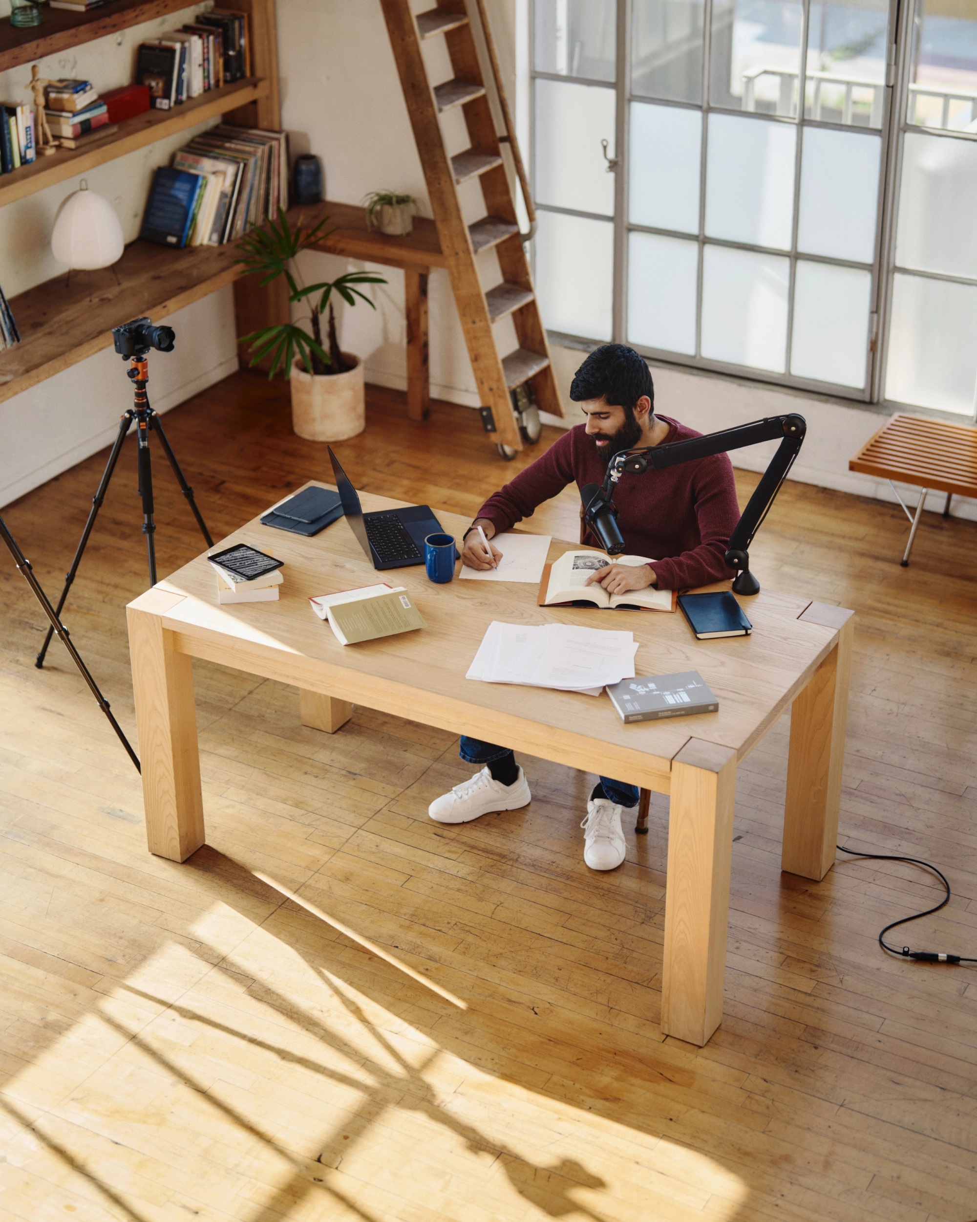 Dwarkesh Patel preparing notes at a table with books, a laptop, and recording equipment
