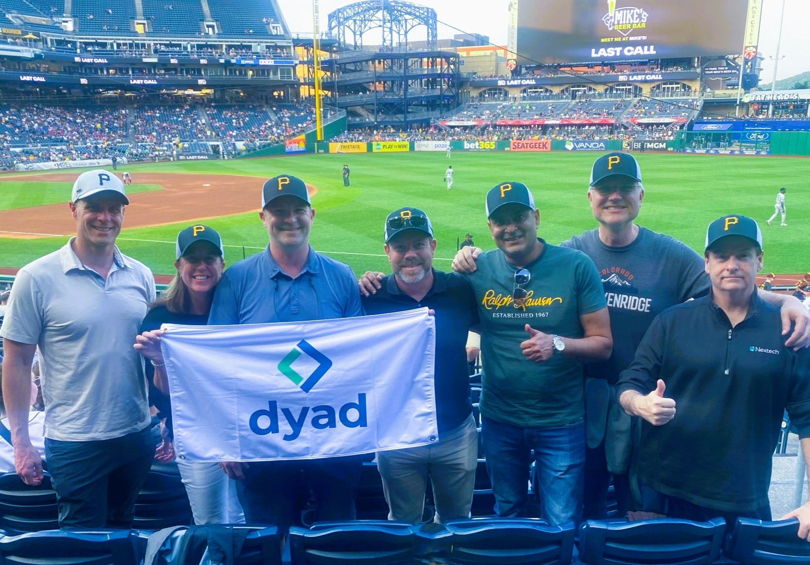 Dyad team members at a Pittsburgh Pirates baseball game holding a Dyad flag