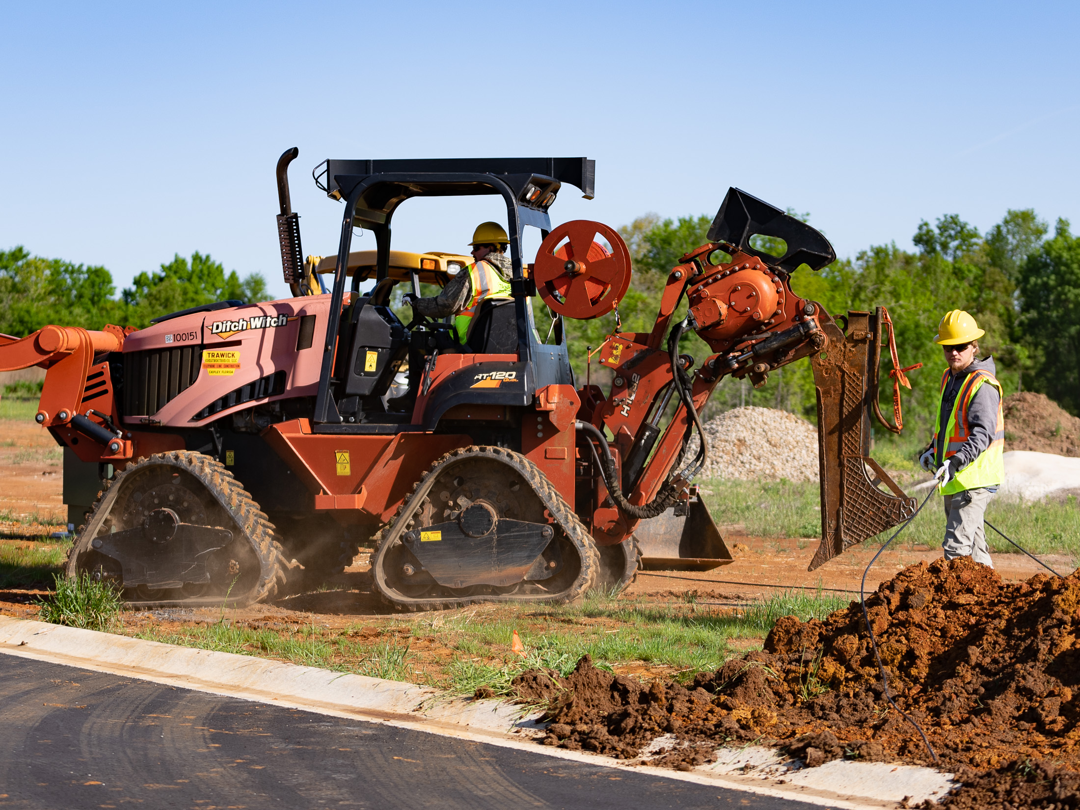 Two construction workers beside an orange Ditch Witch machine at a roadside excavation