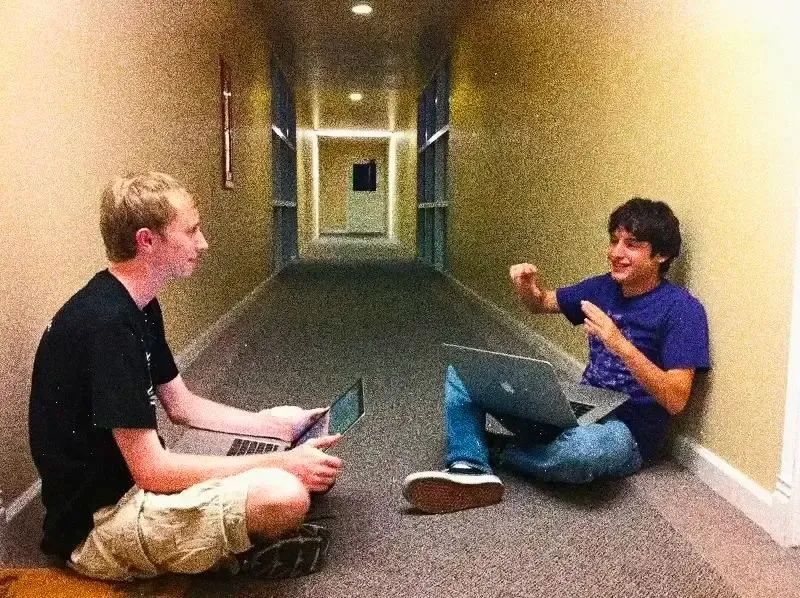 Evan Wallace and Dylan Field seated opposite each other in a hallway, with laptops open
