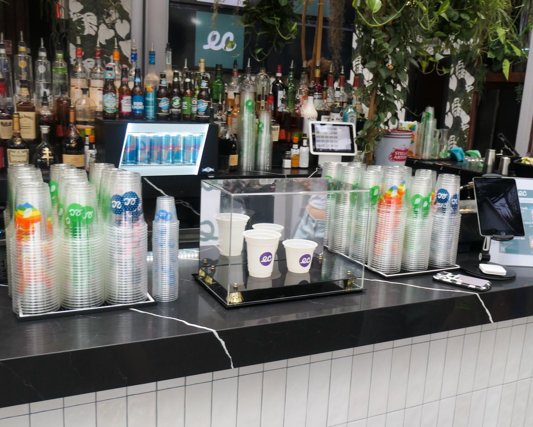 Stacks of clear Earth Cups and paper hot cups on a bar counter