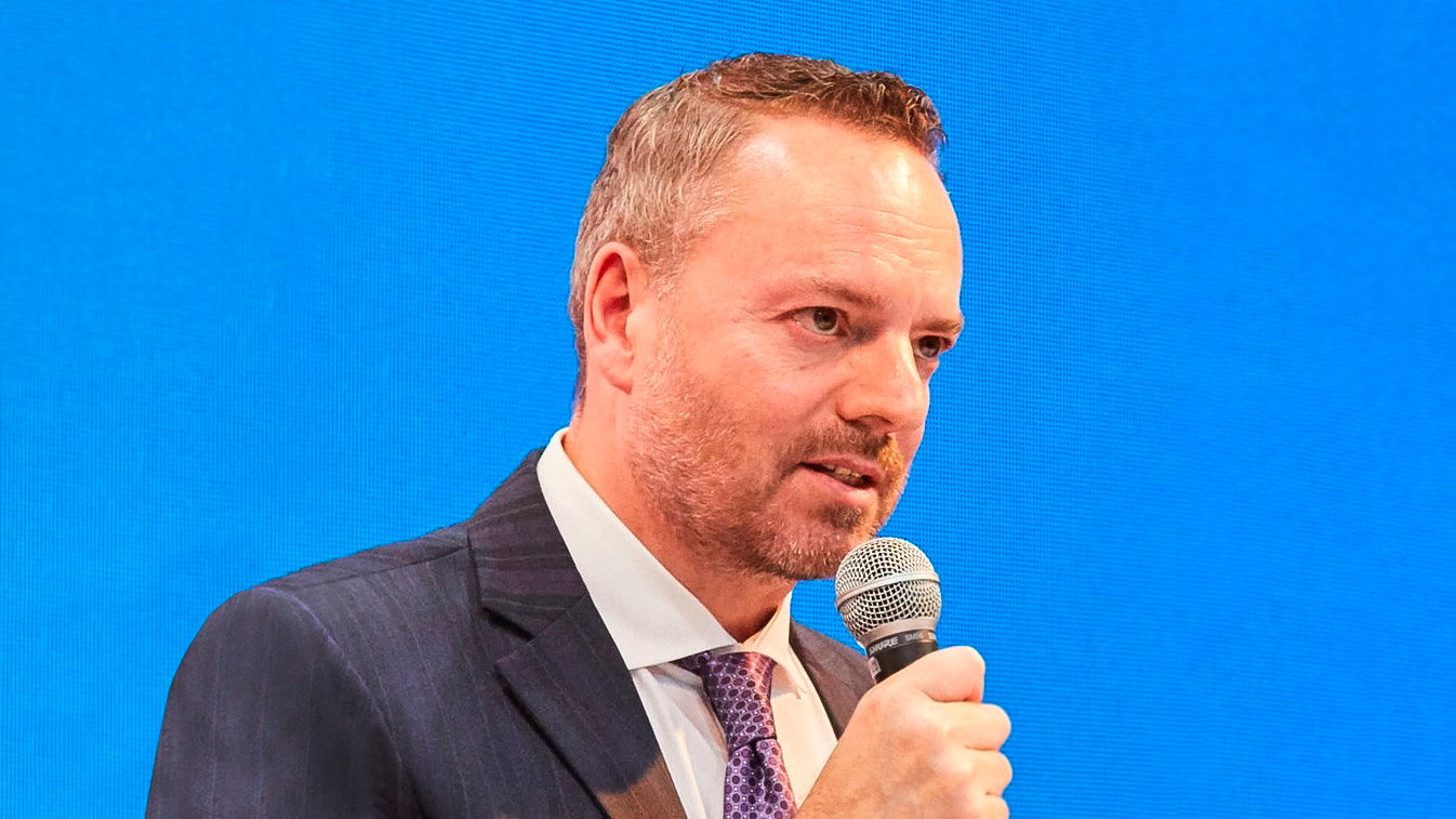 Ed Bowers in a dark suit holding a microphone against a blue stage screen at G2E Asia in Singapore in 2022.