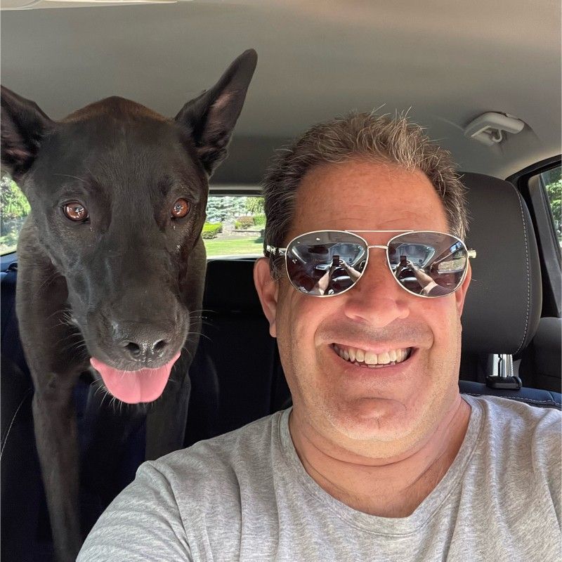Ed Brandman smiling in a car beside Sadie, his Belgian Malinois