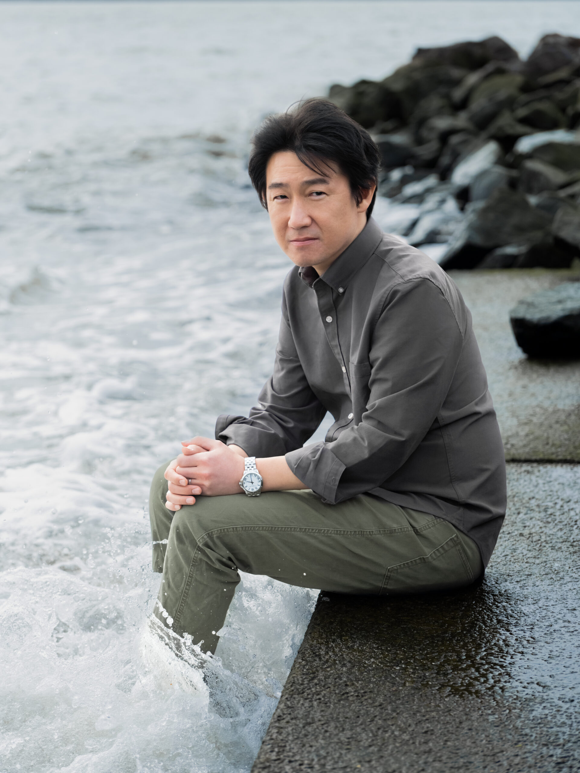 Author Ed Park seated beside the water on a rocky shoreline