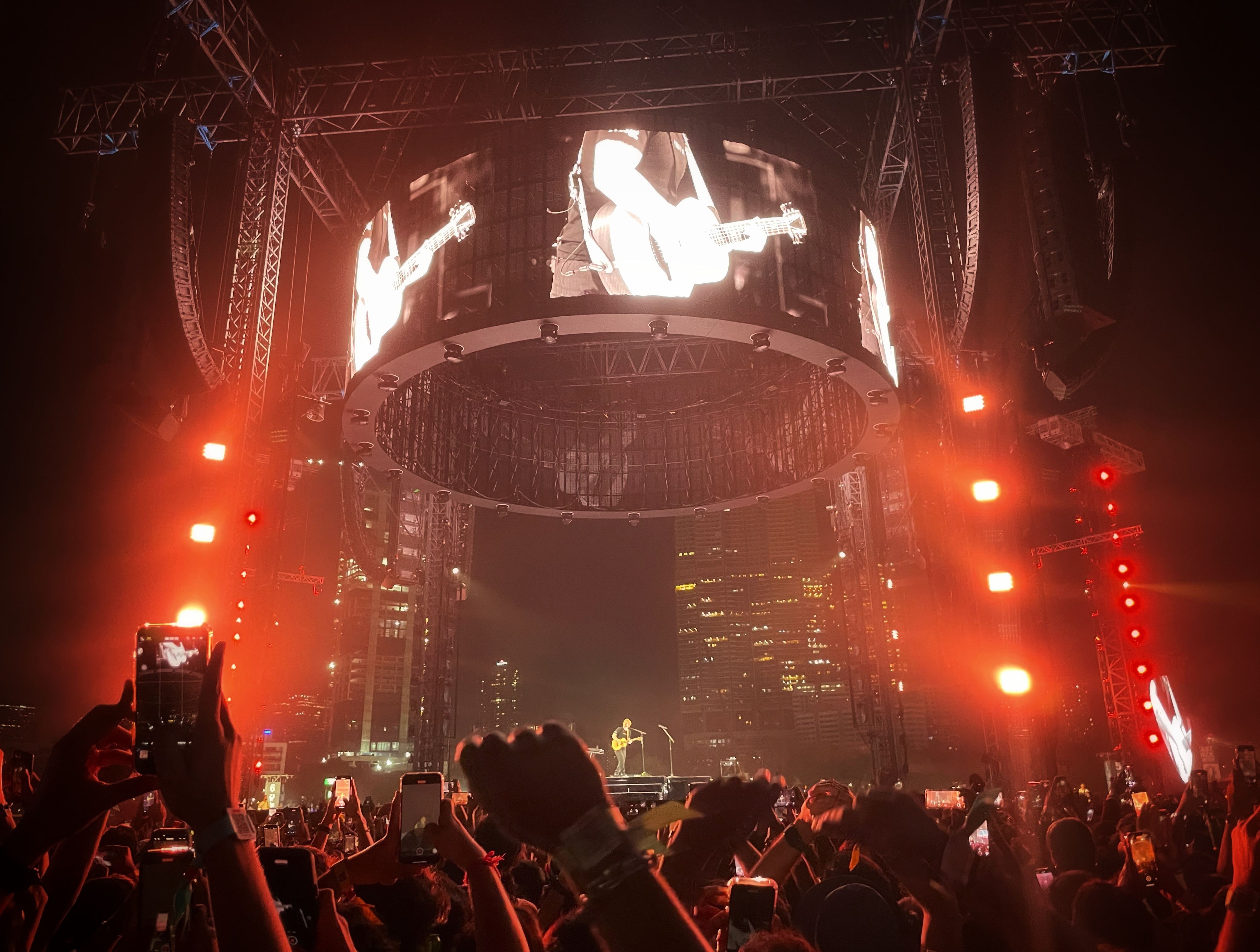 Ed Sheeran performing alone beneath a circular stadium screen in Mumbai