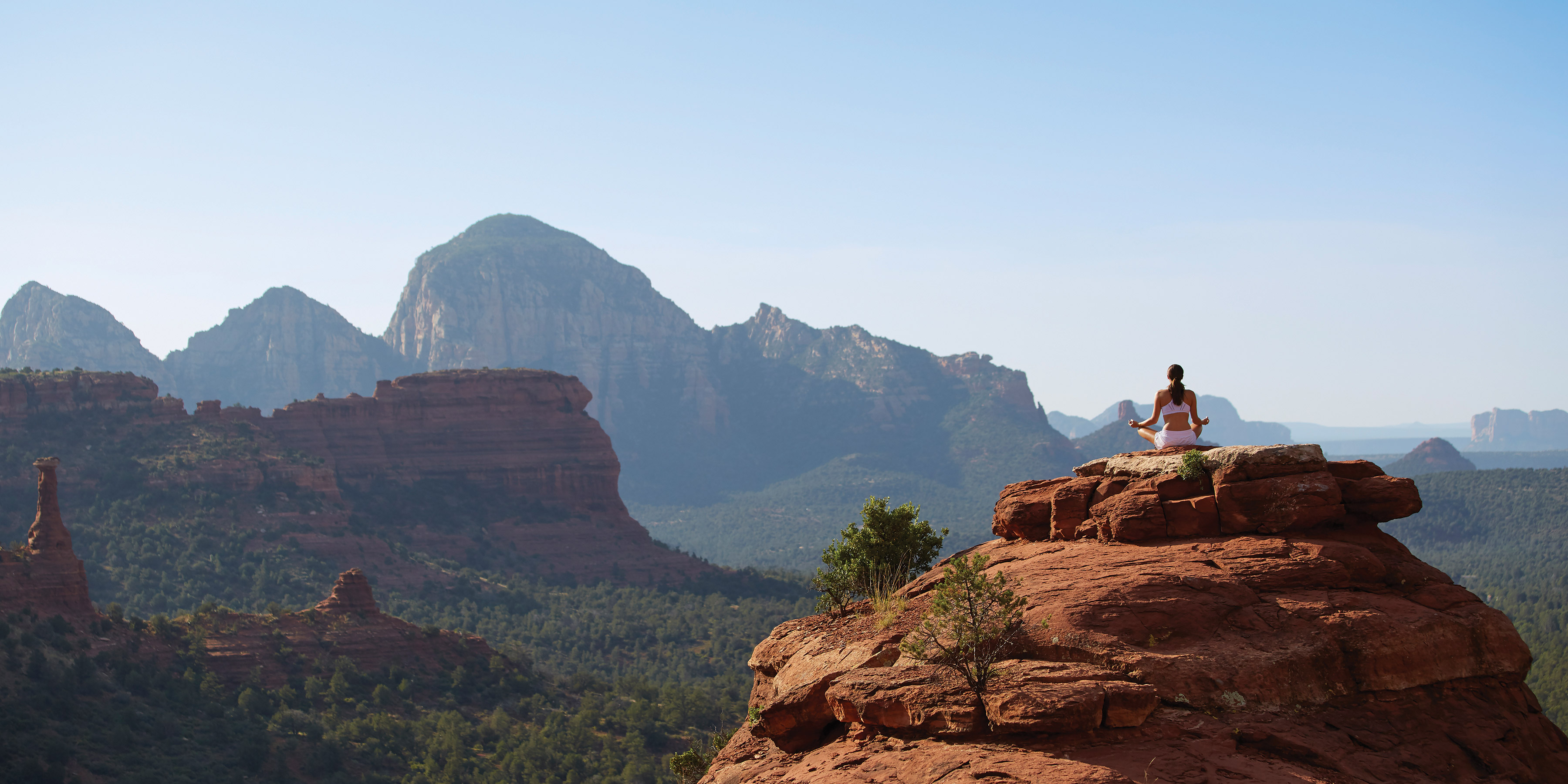 A person meditates on a red-rock outcrop overlooking the Sedona landscape