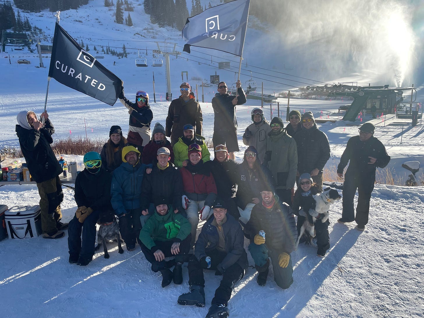 Curated experts gathered outdoors at a snowy ski area with Curated flags