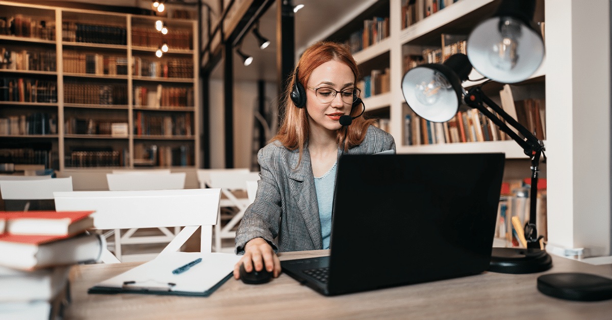 A headset-wearing advisor working at a laptop in a library setting