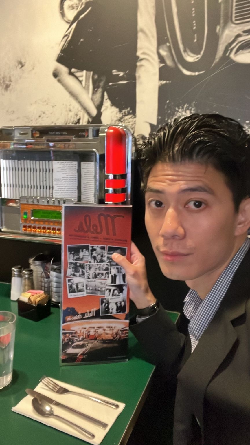 Edward Chiu seated at Mel’s Diner beside a tabletop jukebox, holding the menu