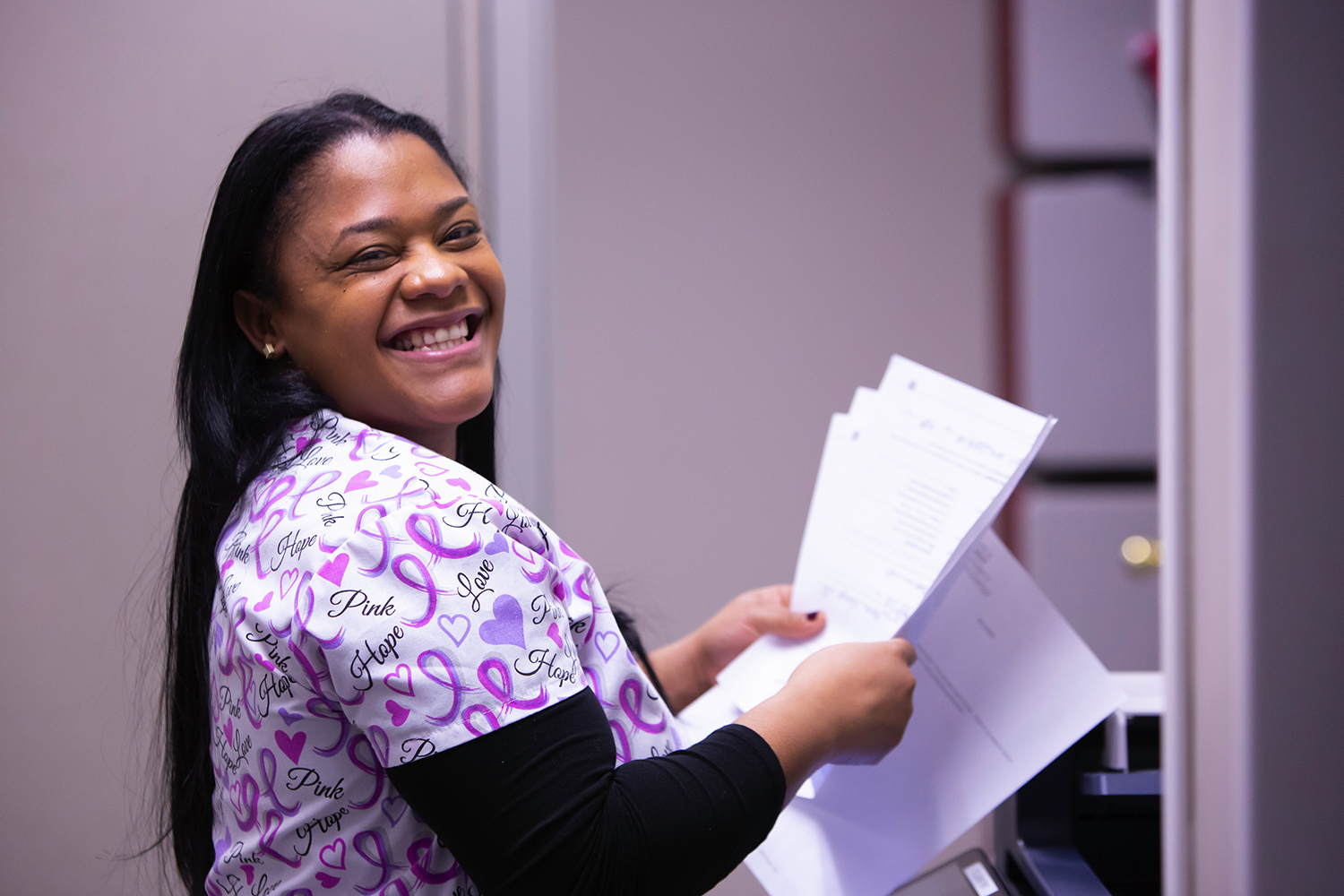 A smiling Kennedy Community Health staff member in patterned scrubs holding paperwork