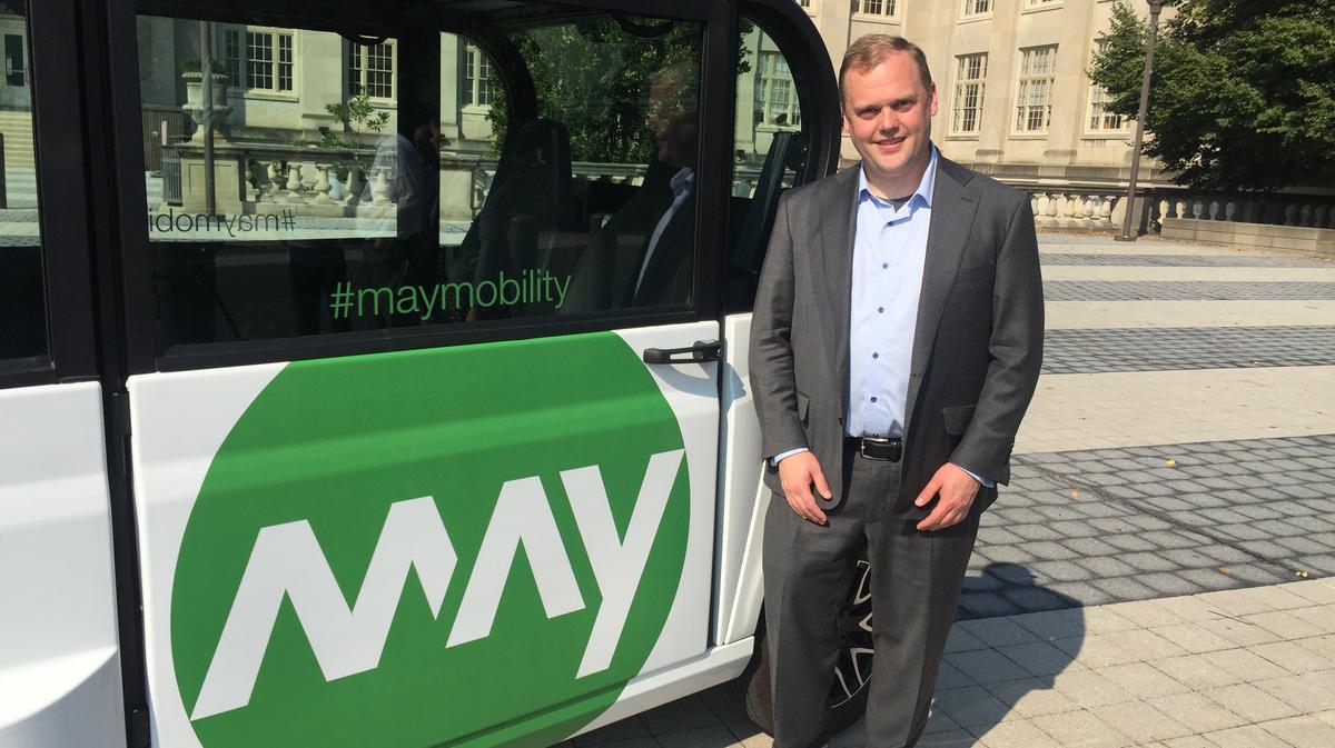 Edwin Olson standing beside an early green-and-white May Mobility shuttle