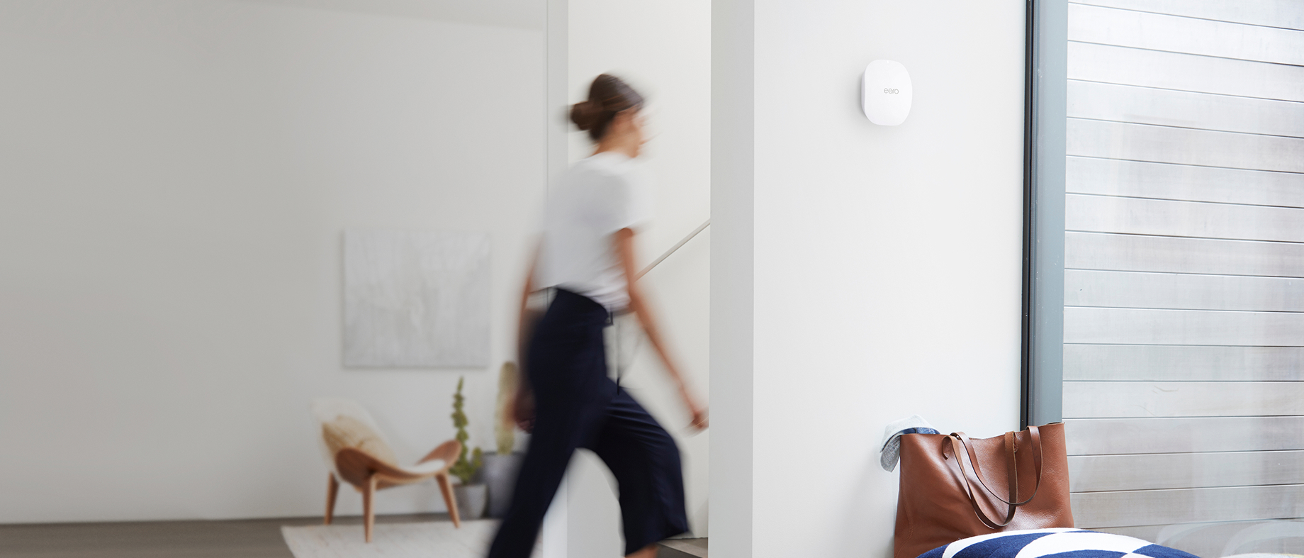 A white eero access point mounted high on a wall in a bright modern room