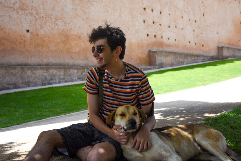 Ege Kaan Duman sitting outdoors in a striped shirt and sunglasses with a dog beside him