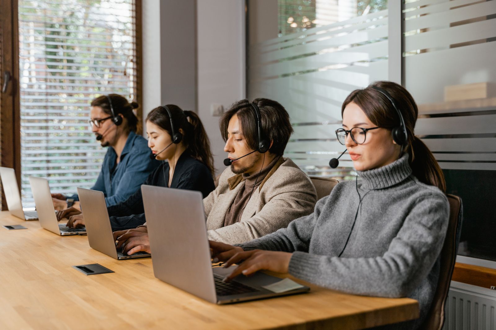 Four customer support specialists wearing headsets and working on laptops in an office
