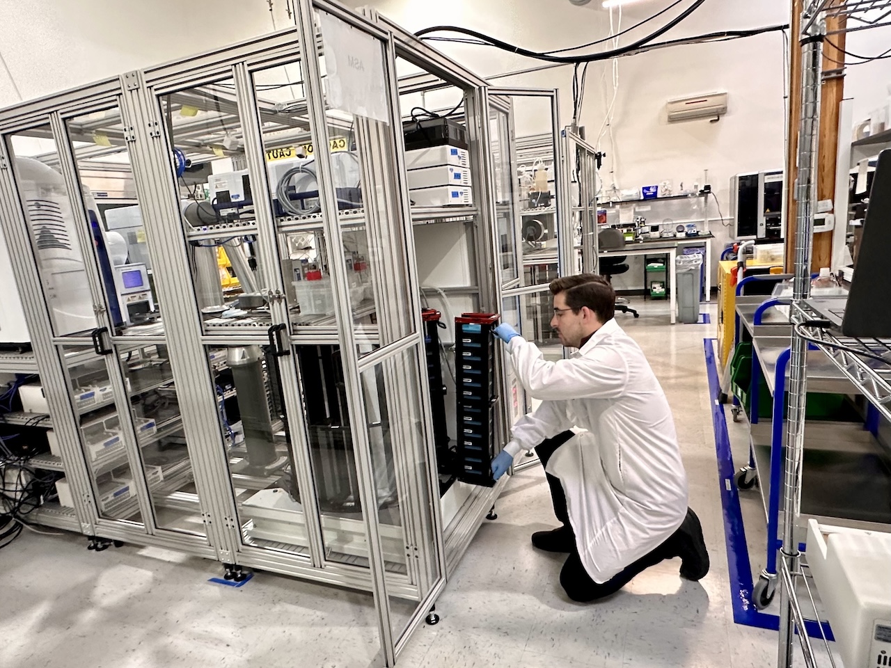An Elegen scientist kneels beside the automated GEN II DNA production system in a laboratory