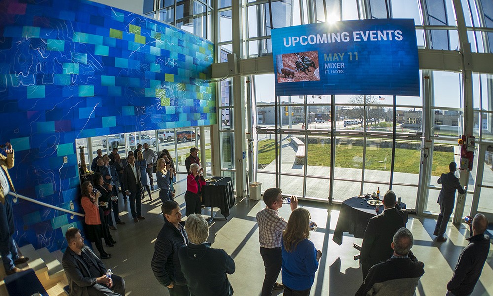 A gathering in the accelerator building’s bright lobby, with a blue wall and floor-to-ceiling windows