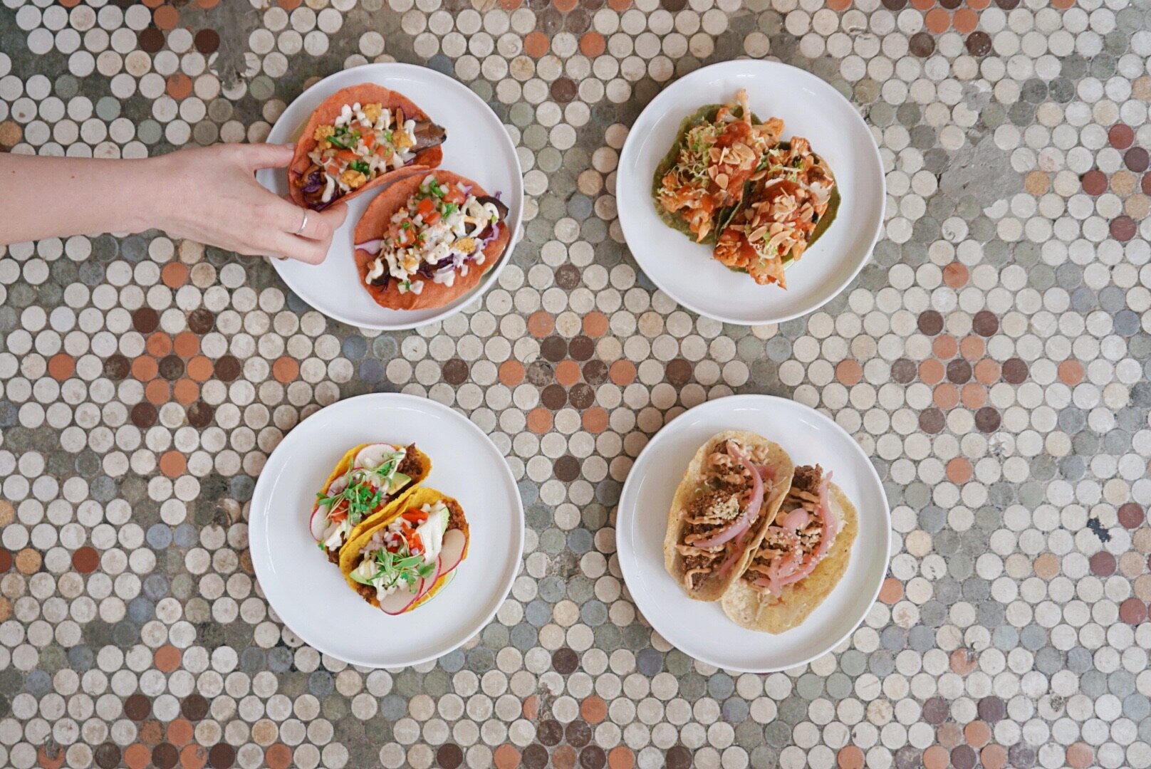 Four colorful plates of tacos arranged on a tiled restaurant floor