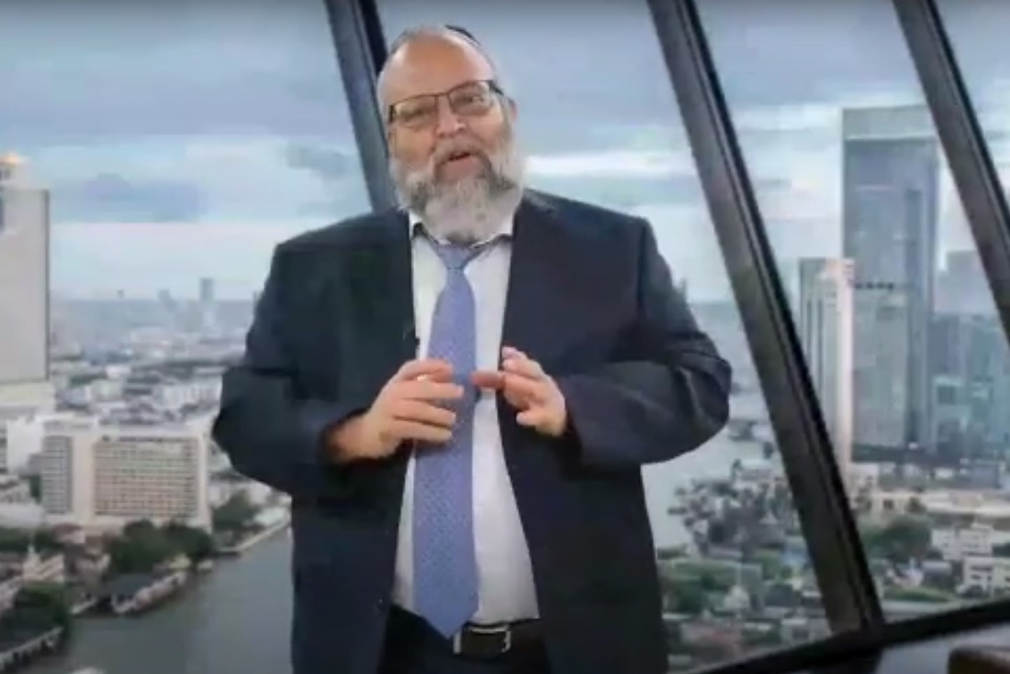 Eli Gross speaking in a Besadno interview, gesturing with both hands in front of large windows
