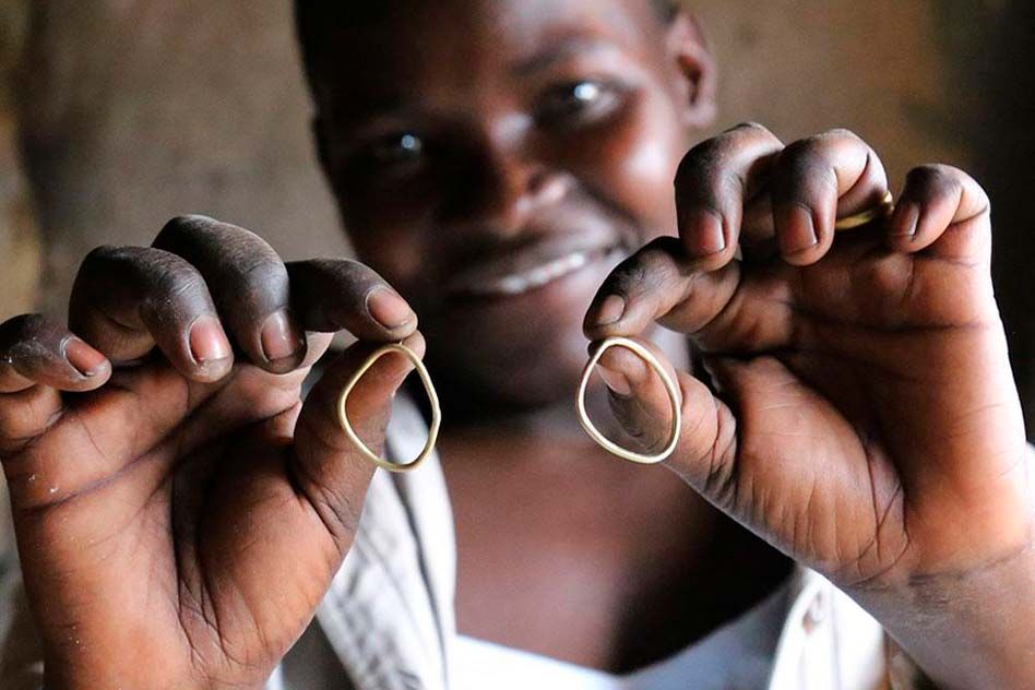 A SOKO artisan holds up two brass jewelry pieces