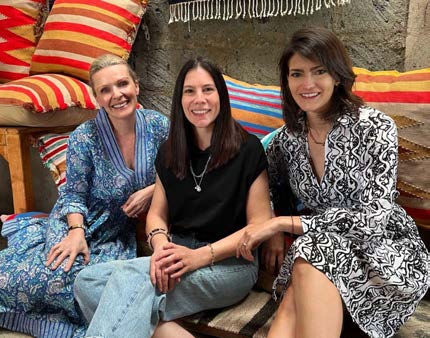 Powered by People co-founders Hedvig Alexander, Alison Phillips, and Ella Peinovich seated together among colorful textiles