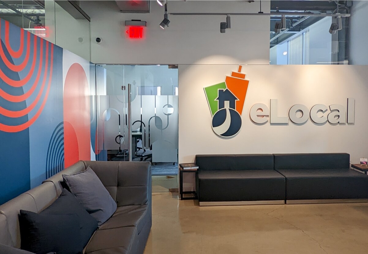 eLocal’s Conshohocken office reception with sofas, glass meeting rooms and its wall sign