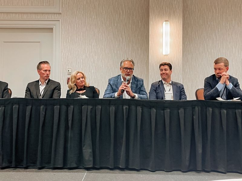 Elroy Gust, centre, holding a microphone among panellists at the 2024 Pinnacle Wealth Brokers Conference in Kelowna