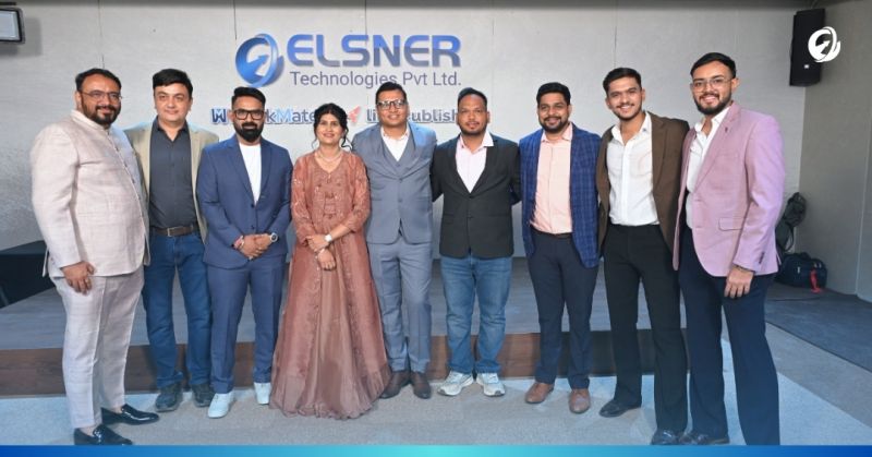 Nine people pose together beneath Elsner Technologies signage at a company gathering.