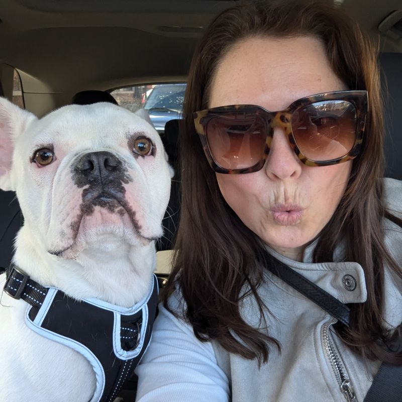 Emily Hite wearing sunglasses beside her white dog in a car