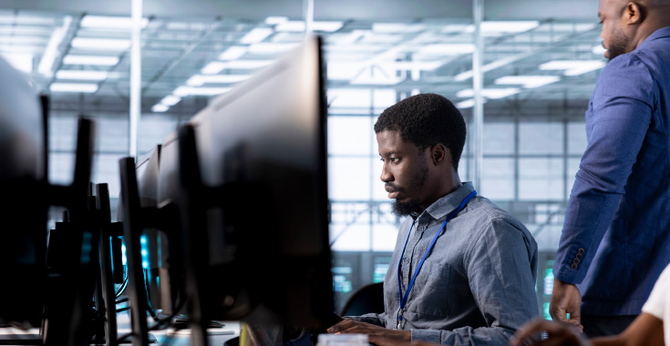 An operator studying a desktop monitor, from the Emovis Verify product page
