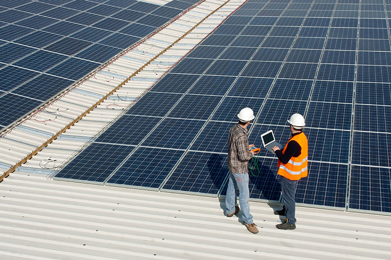 Two solar professionals inspecting a large commercial rooftop array