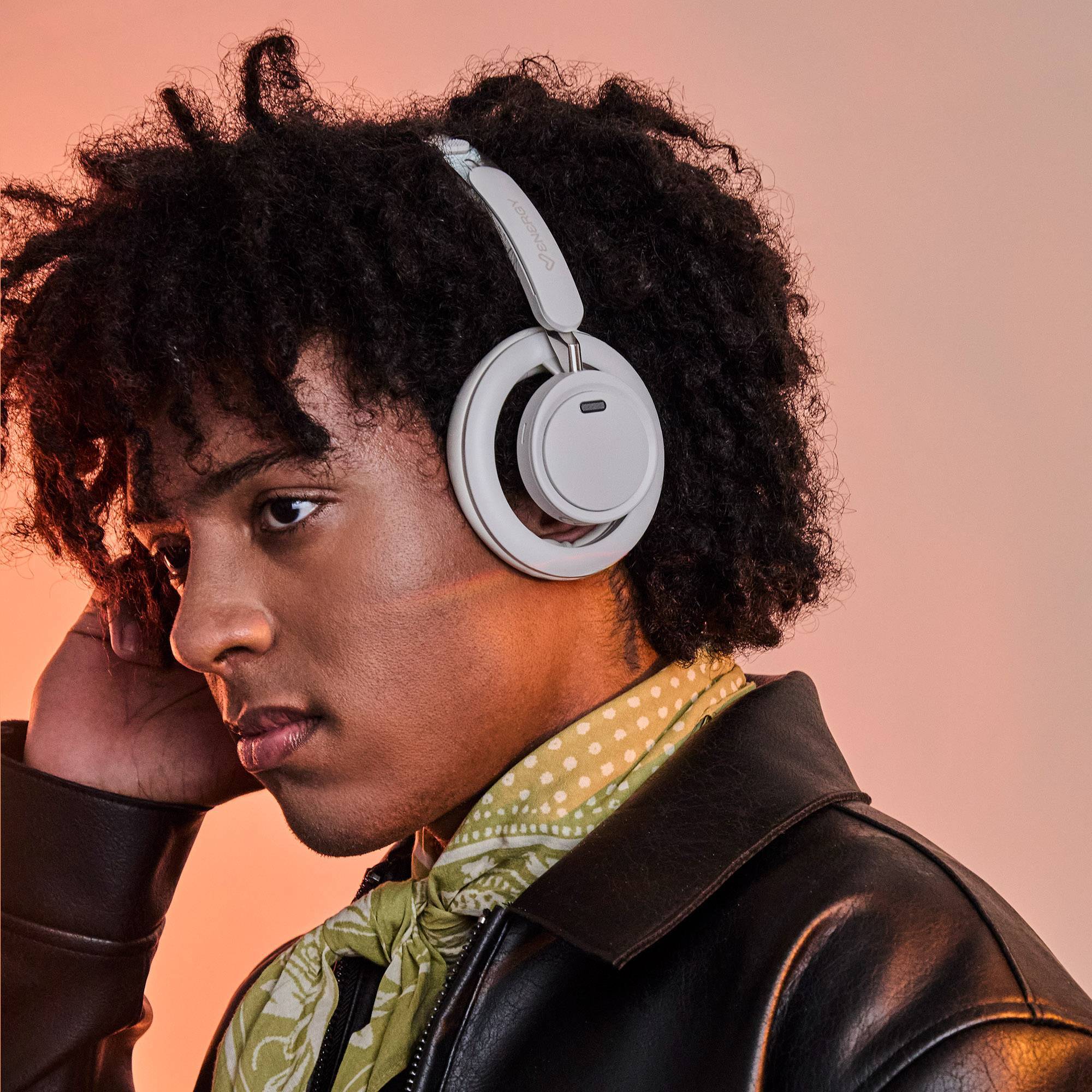 Model wearing white Energy Sistem over-ear headphones against a warm peach background