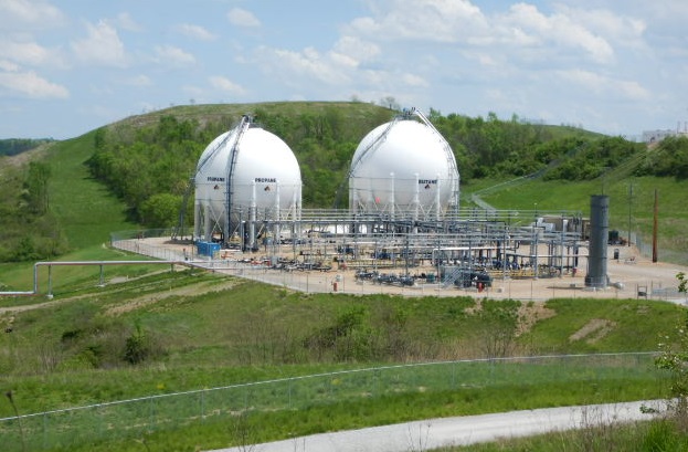 Two white propane storage spheres surrounded by pipes and green embankments
