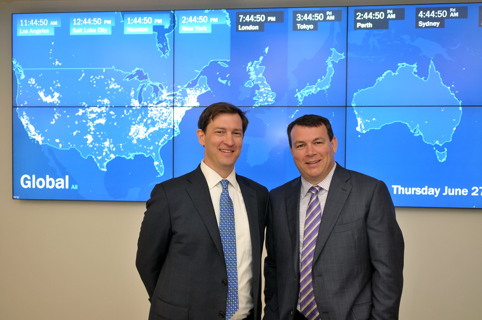 Two men at an EnerNOC ribbon-cutting event in front of a wall of international operations displays