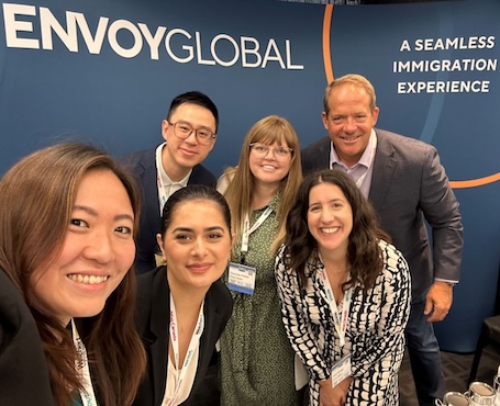 Six people posing together in front of an Envoy Global event display
