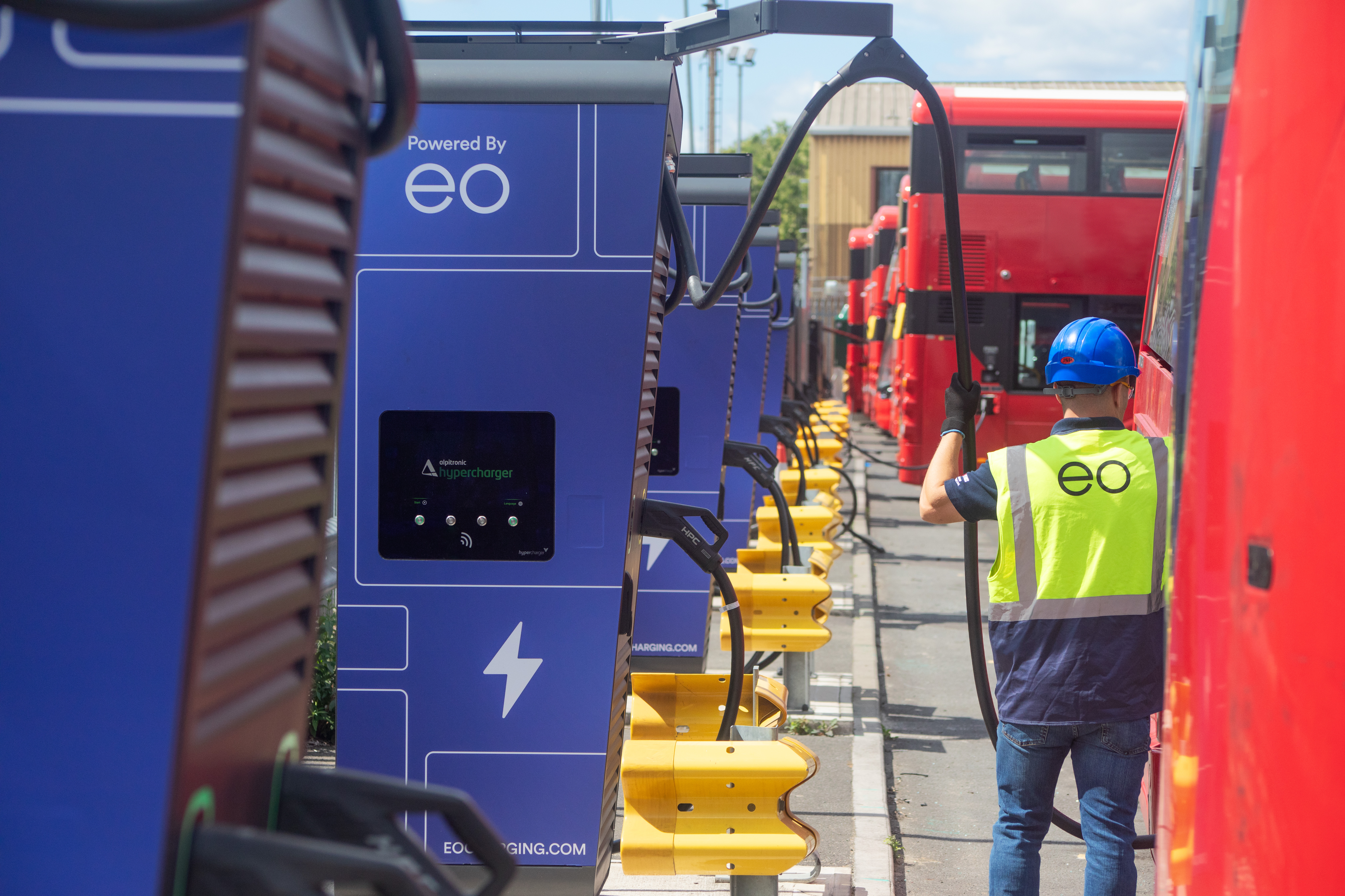 An EO Charging engineer connects a blue high-power charger to a red electric bus at a depot