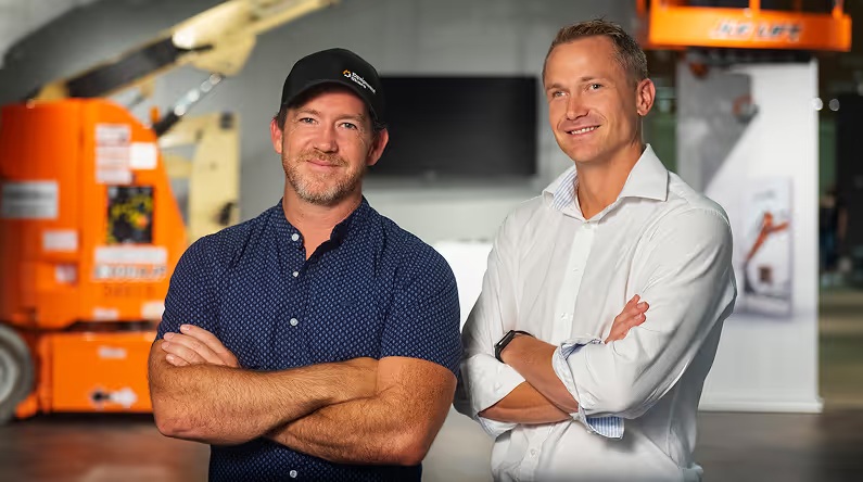 EquipmentShare founders Jabbok and Willy Schlacks standing in front of construction equipment