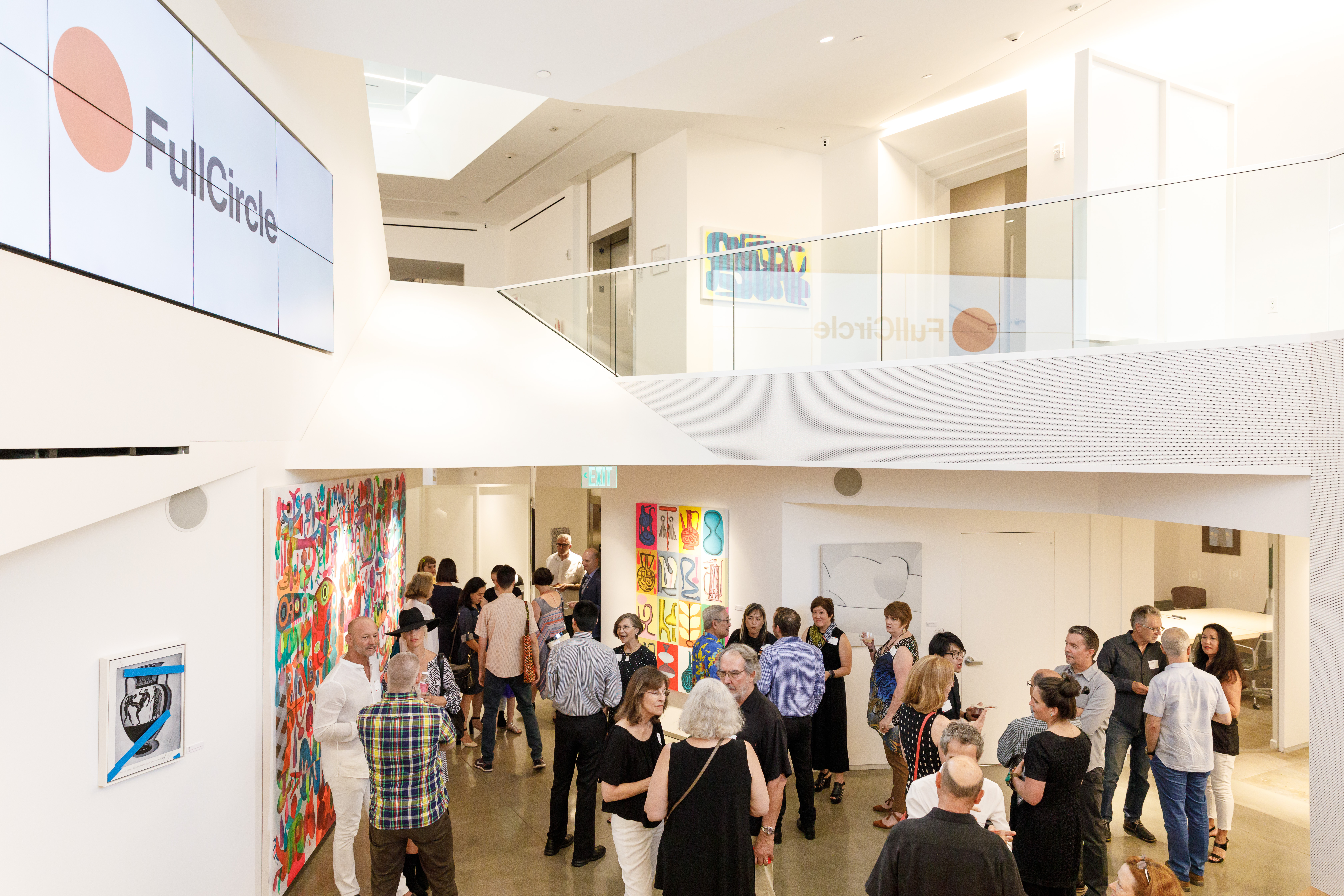 Guests talking among paintings in the bright, two-level sp[a]ce gallery