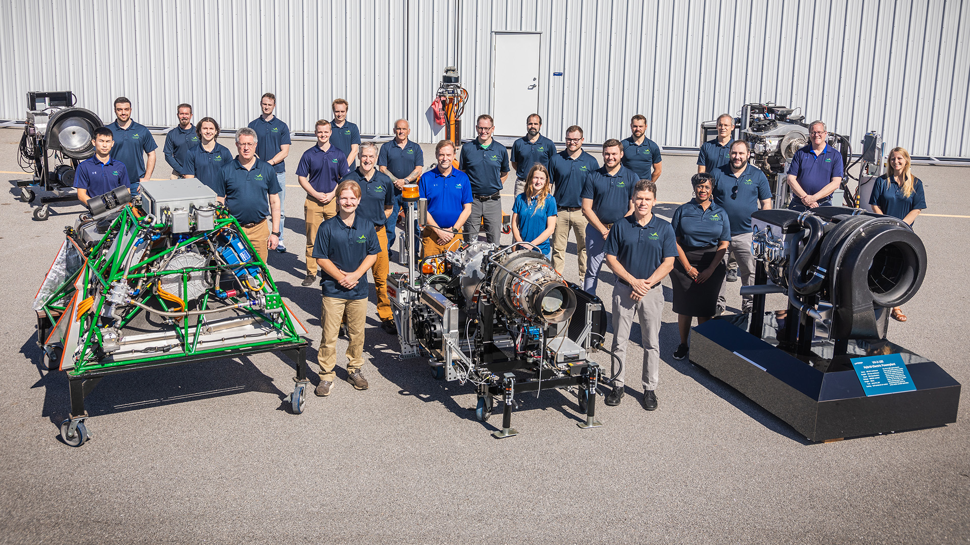 The VerdeGo Aero team standing outdoors among three hybrid-electric powerplant test rigs